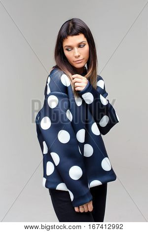 Nice thoughtful model close-up looking aside in studio with grey background, she is wearing dark blue polka dots costume, her head is slented and eyes are looking aside