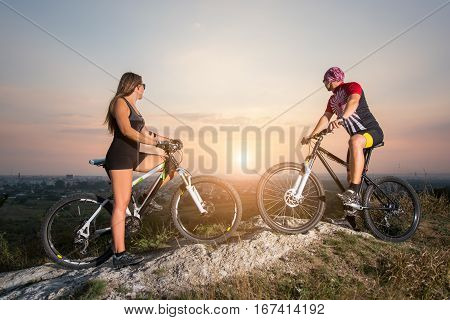 Cyclist Couple With Mountain Bikes On The Hill At Sunset