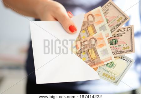 Woman handing out an envelope stuffed with euros and US dollar banknotes as bribe