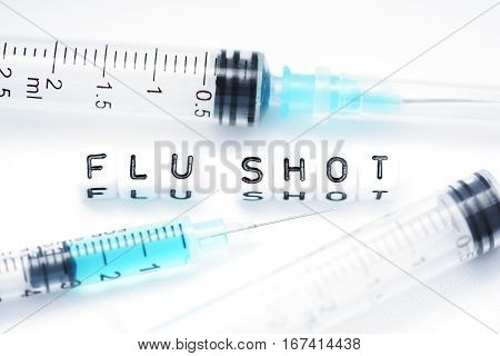 Flu shot text spelled with tiled plastic letters standing next to a syringe