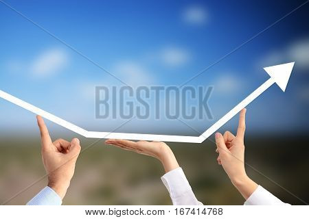 Business people's hands holding an up going arrow suggesting the benefits of teamwork on an agricultural field background