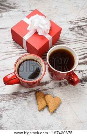 two red coffee cup, hearts cokies and gift box on wooden surface. Valentines day concept.