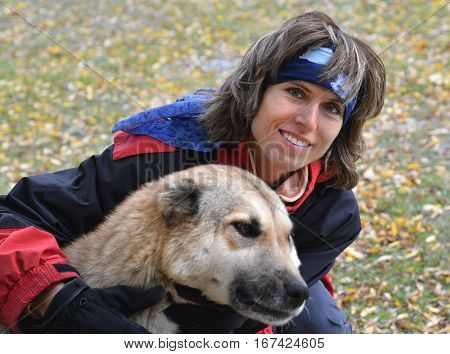 Happy woman holds Caucasian Shepherd dog. Outdoor scene. Meadow with yellow leaves in background.