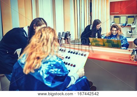 beauty hair dyeing and people concept - happy young woman with hairdresser choosing hair color from palette samples at salon