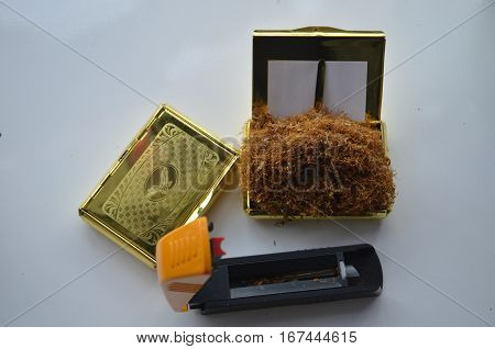 machine for filling cigarettes on the table with yellow lid and some tobacco in it and a snuffbox with tobacco in it