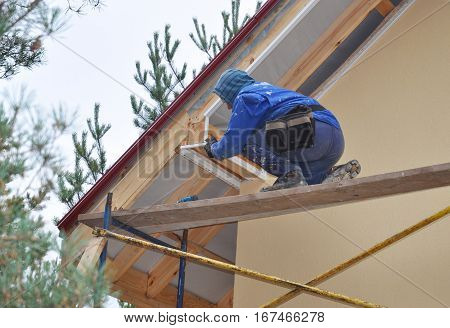 KYIV UKRAINE - February  14 2017:  Roofer on the Corner of House Install Soffit. Roofing Construction. Soffit is Usually Constructed of Vinyl Wood or Aluminum and is Installed on the Underside of Roof Overhangs and Eaves.