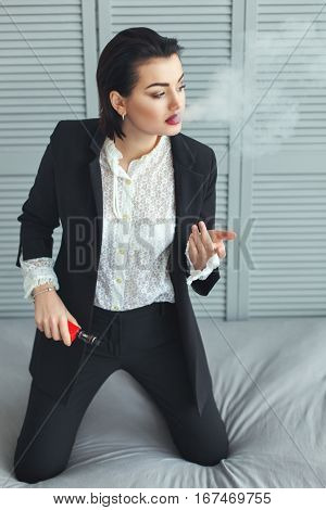 Woman in a business suit smokes electronic cigarette.