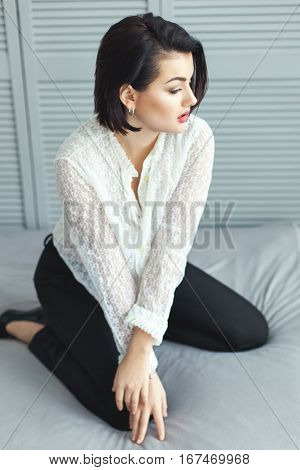 Woman in diaphanous shirt on the bed in the bedroom.