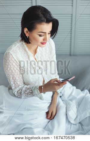 Pretty woman in the morning in bed reading a message on your phone.