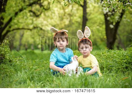 Two Little Kids Boys And Friends In Easter Bunny Ears During Traditional Egg Hunt In Spring Garden,