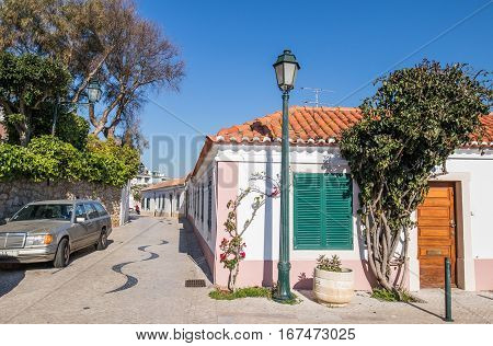 Beautiful typical rebuilt portuguese house in a village called cascais. with a pink frame in a sone made street surrounded by a garden and under the clear blue sky.