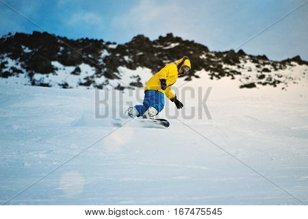 Man rides his snowboard very fast, making carved turns on frontside edge, on ski slope in winter mountains, in ski resort