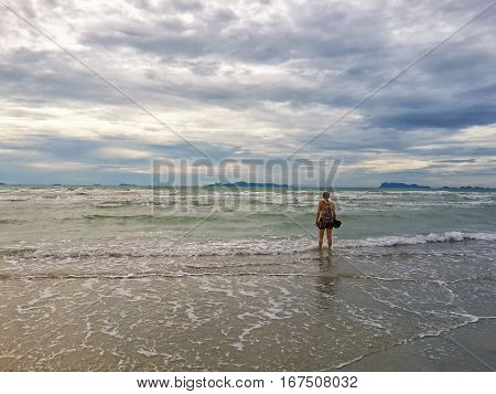 Girl with backpack on the shore of the sunset sea on the incoming wave. Koh Samui Thailand