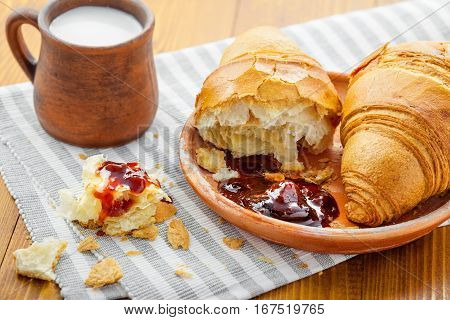 Croissant with fruit jam and fresh milk for breakfast. Delicious French meal on a table.