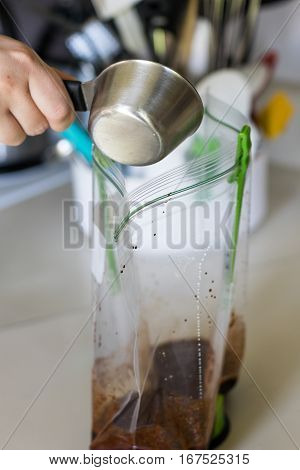Woman pouring ingredients in plastic bag of marinade.