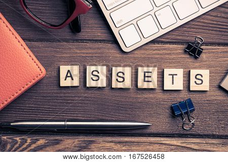 Workspace desk with keyboard office working stuff and wooden elements with the letters collected in the word assets