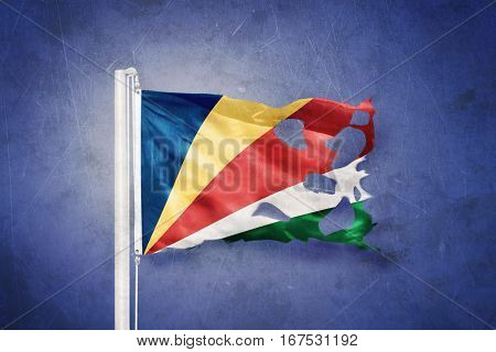 Torn flag of Seychelles flying against grunge background.