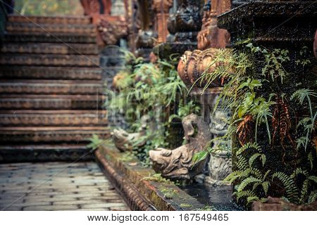Ancient Asian style garden alley with old column overgrown with tropical plants and blurred background
