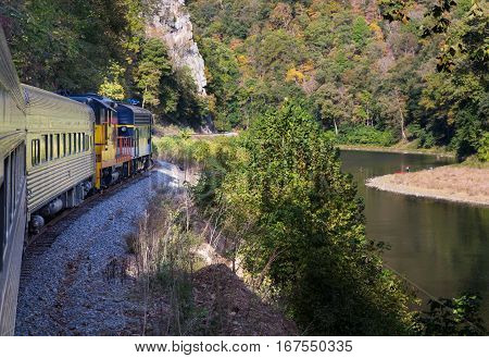 Diesel locomotive engine on steep trip into mountains of West Virginia with fisherman in the calm river below the tracks