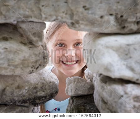 Pretty young girl smiling at the camera through an opening in a rock wall.