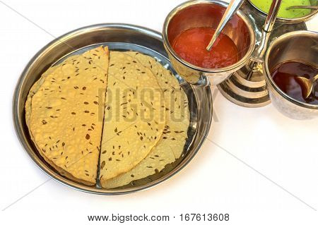 Indian bread served with the traditional assortment of sauces, in the typical tableware, on a white background. Selective focus