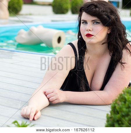 Young beautiful busty curvy plus size model with big breast in black bra professional makeup and hairstyle lying near the outdoors pool