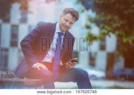 Portrait of handsome businessman holding mobile phone while sitting on bench