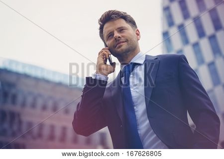 Low angle view of smart businessman talking on mobile phone against office building