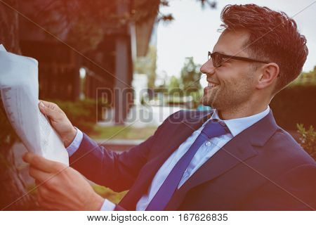 Close up of cheerful businessman reading newspaper in yard