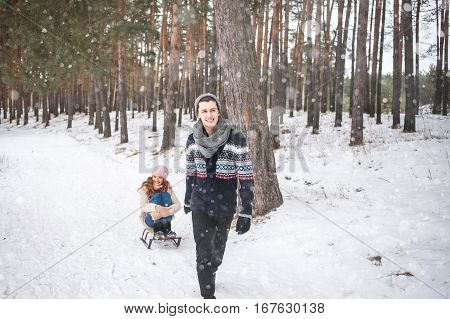 Young couple walking and sledding in the winter in the forest during a snowfall