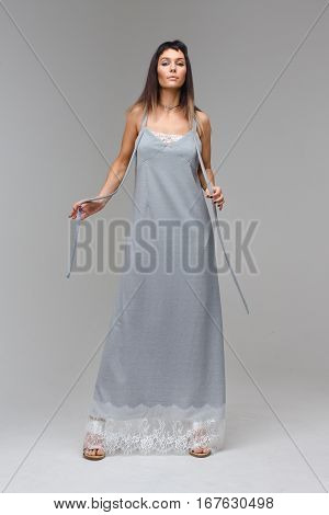 Nice prideful model wearing long grey lace nighty standing in studio with grey background looking to the photograther with open hands