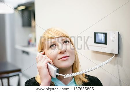 Smiling Blonde Woman Answers The Intercom Call, Hold The Phone To His Ear, Waiting For The Arrival O