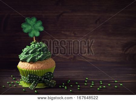 Cupcake with clover cakepick on a wooden background