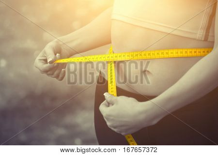 Sport girl measuring waist with yellow measuring tape. Reducing excess weight. Healthy lifestyle.