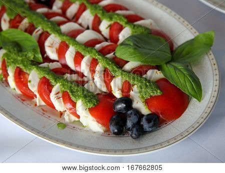 Caprese salad with tomatomozzarella bazil and pesto on a dish. Selective focus