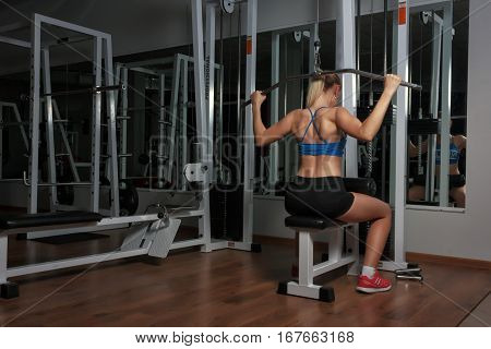 Color photo of a strong woman from behind. Blonde sexy fitness girl in sport wear with perfect body in the gym posing before training set. Attractive fitness woman, trained female body