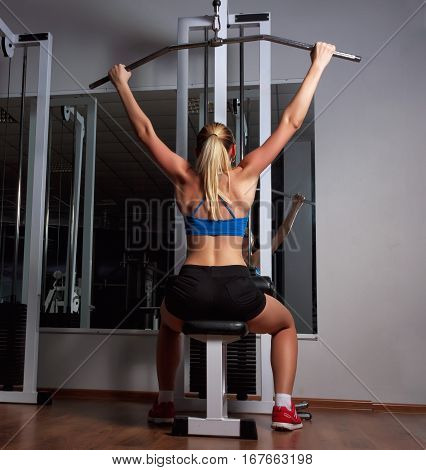 Girl trains the back muscles on the sports simulator in fitness club