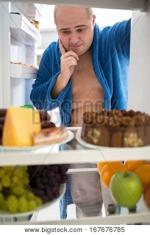 Fat guy think what to eat healthy or tasty food from refrigerator