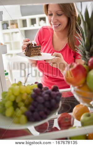 Young woman take nice piece of chocolate cake from refrigerator