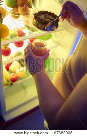 Corpulent male eatat night jam from jar with spoon