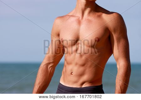 Torso of young muscular man at the sea. Sculpted abs and athletic body.