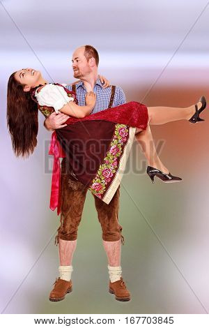 Bavarian man in leather pants wears his girlfriend in the Dirndl Dress on the poor.