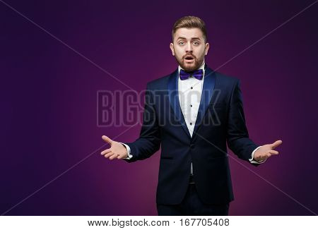 Handsome man in tuxedo and bow tie is surprised and throws his hands. compere in fashionable, festive clothing on dark background