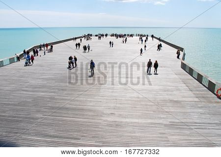HASTINGS, ENGLAND - APRIL 30, 2016: People walk on the newly restored Victorian pier. Built in 1872, the pier was badly damaged by fire in October 2010 and was finally reopened in April 2016.