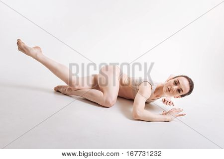 Grace in every step. Gracile airy young ballet dancer performing isolated in the white colored room and lying on the floor while expressing elegance and taking part in the art performance