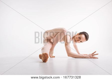 Creativity of every motion. Gracile flexible powerful dancer performing isolated in the white colored studio and lying on the floor while expressing elegance and taking part in the art performance