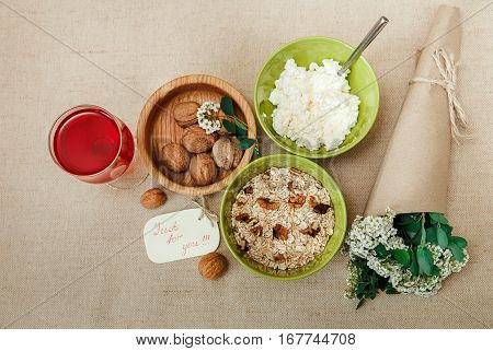 Healthy Organic Breakfast.Walnuts,Oatmeal andC ottage Cheese.Green Ceramic and Wooden Plates.Glass with Red Drink.Wish Yellow Card with Bouquet.Top View