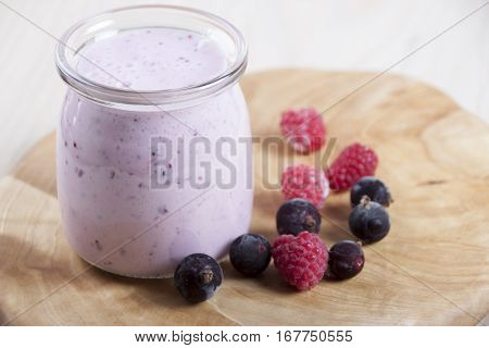 Smoothies with frozen berries black currants and raspberries in jar on a wooden stand.