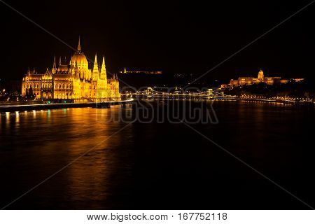 Hungarian Parliament Building Located At The Bank Of The Dunabe River With Famous Chain Bridge Conne