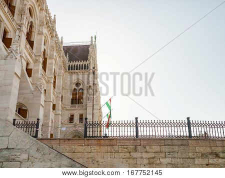 National Flags Handing On Hungarian Parliament Building Located At The Bank Of Dunabe River In Budap